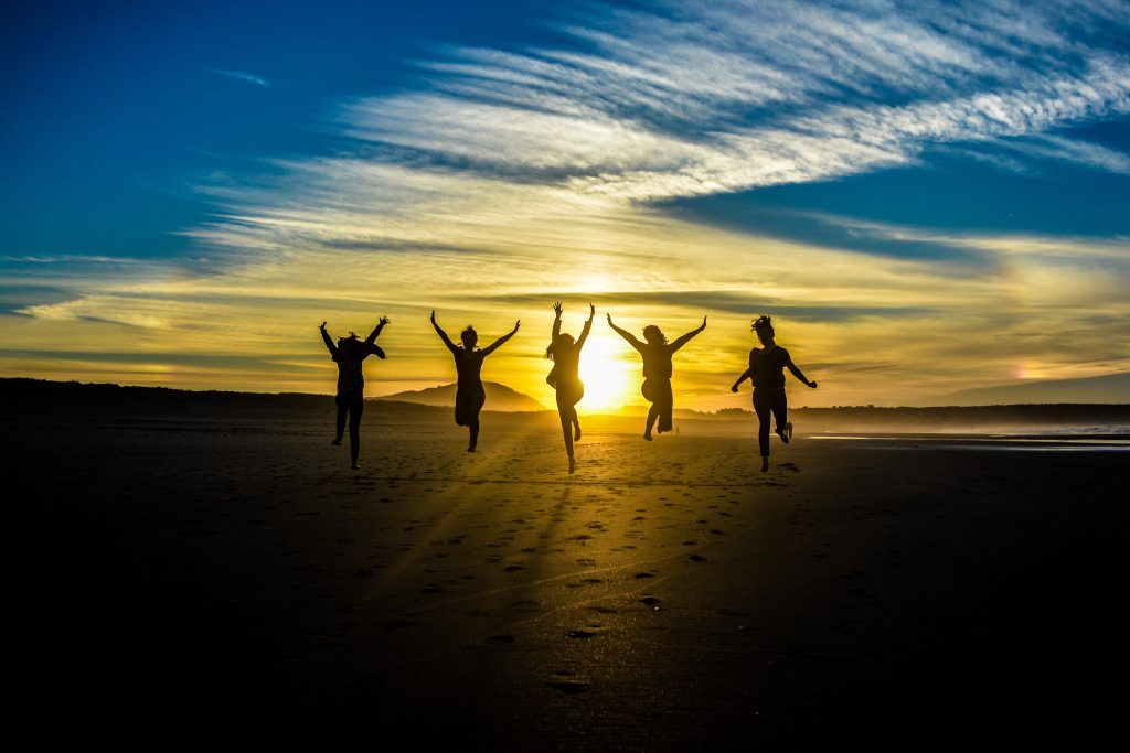 Five people jumping up in the air with the sun setting behind