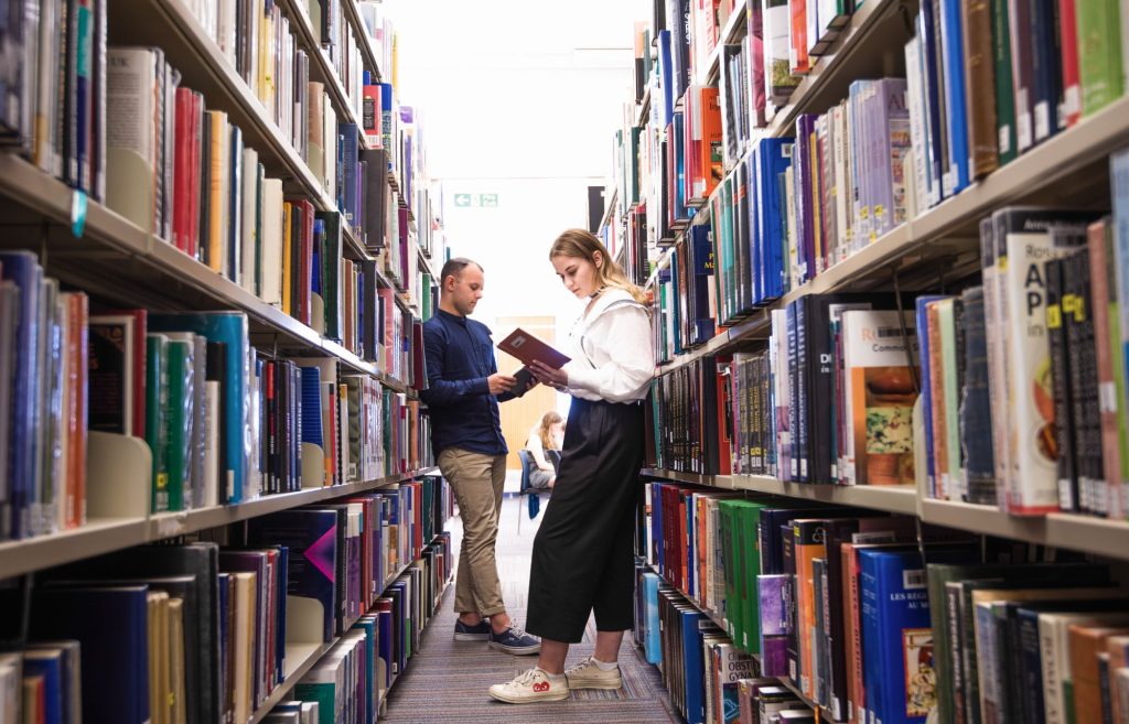 Students leaning against bookshelves reading books
