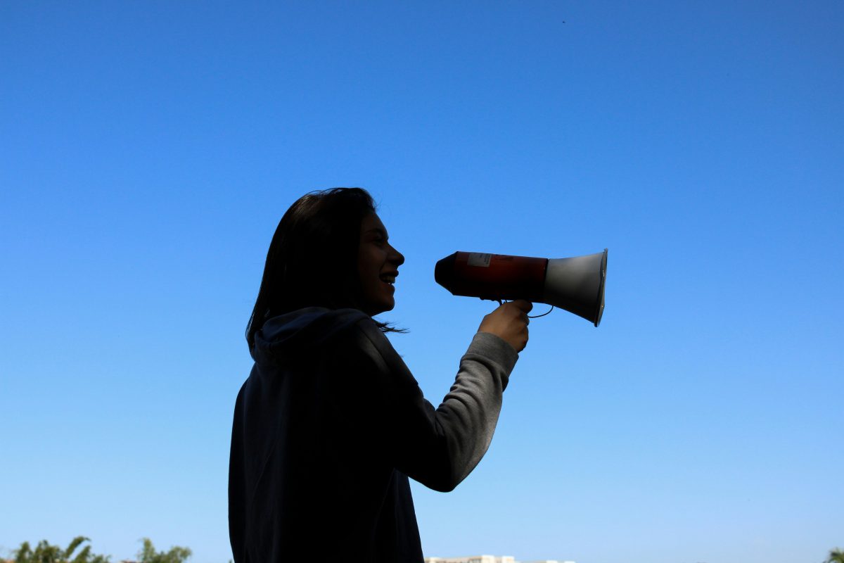 A silhouette of a person shouting into a hand held loudspeaker against the back ground of a blue sky