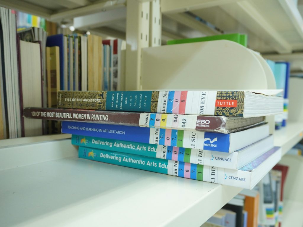 Five books laid flat on a shelf on top of each other. 