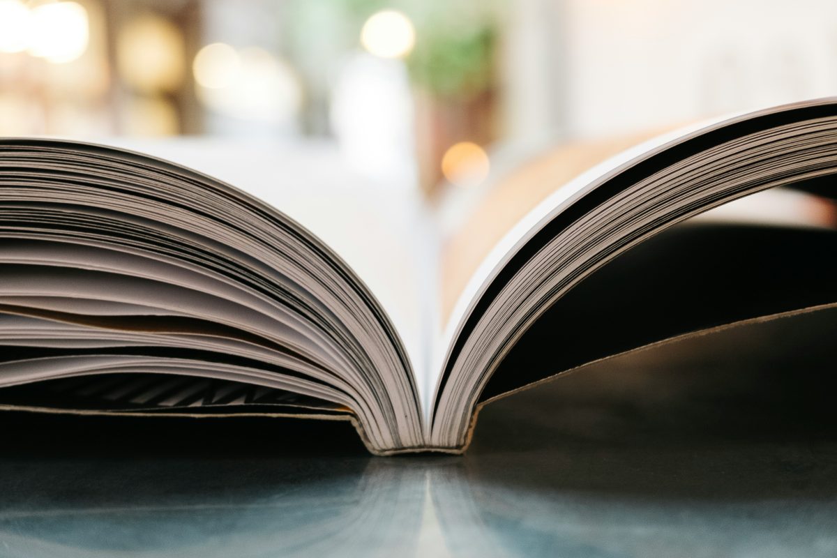 An open book which is reflected in a shiny bue surface. The background is blurry.book